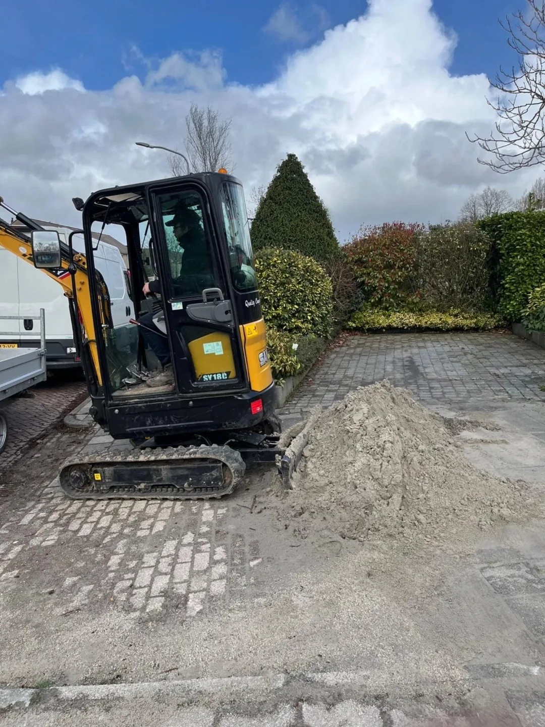 Minigraver verplaatst zand op een oprit naast een woning